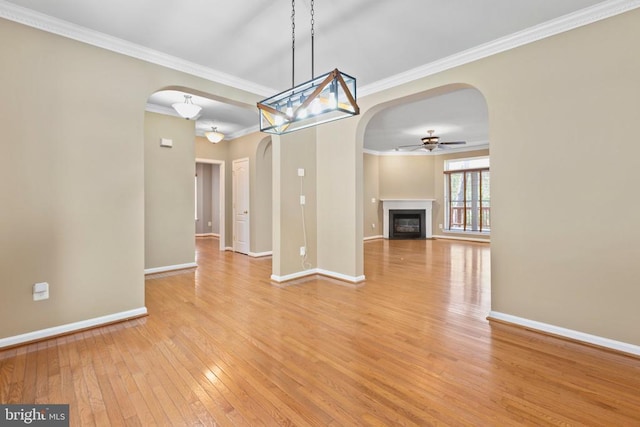 unfurnished dining area with arched walkways, light wood-type flooring, a ceiling fan, baseboards, and ornamental molding