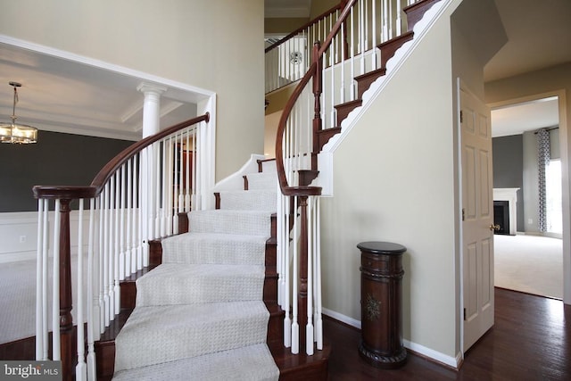  - stairway featuring wood finished floors, crown molding, a chandelier, and a fireplace