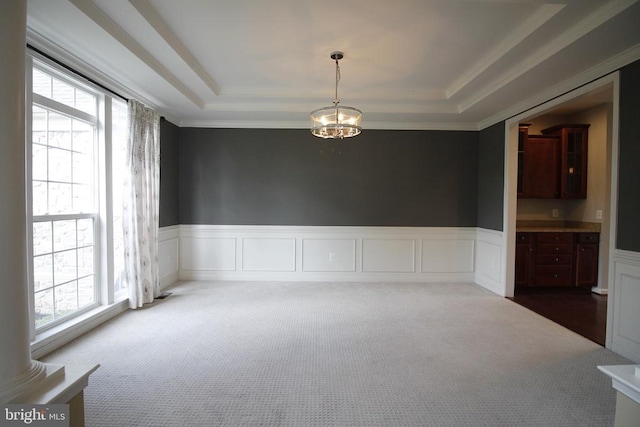  - empty room with dark colored carpet, a raised ceiling, a wainscoted wall, crown molding, and a chandelier