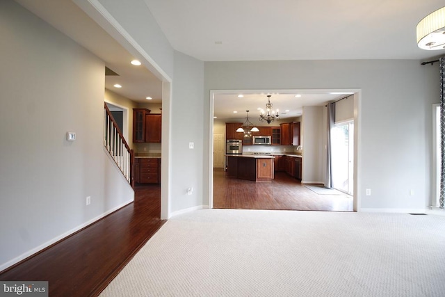  - unfurnished living room featuring a chandelier, carpet floors, recessed lighting, stairs, and wood finished floors