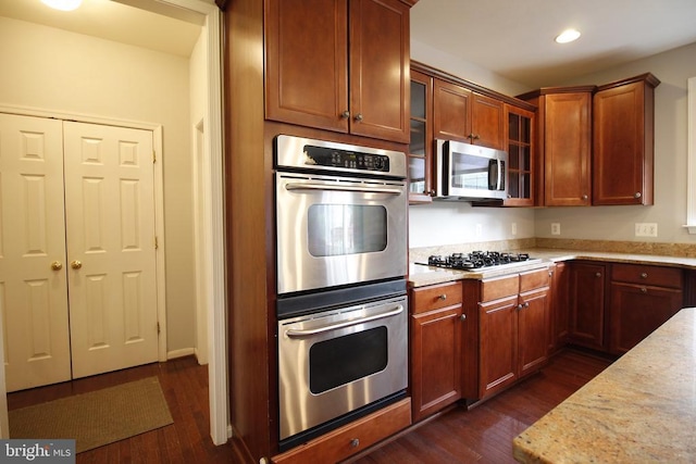  - kitchen with appliances with stainless steel finishes, dark wood finished floors, recessed lighting, glass insert cabinets, and light stone countertops
