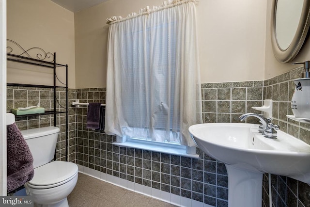 half bathroom with tile walls, tile patterned flooring, a wainscoted wall, and toilet