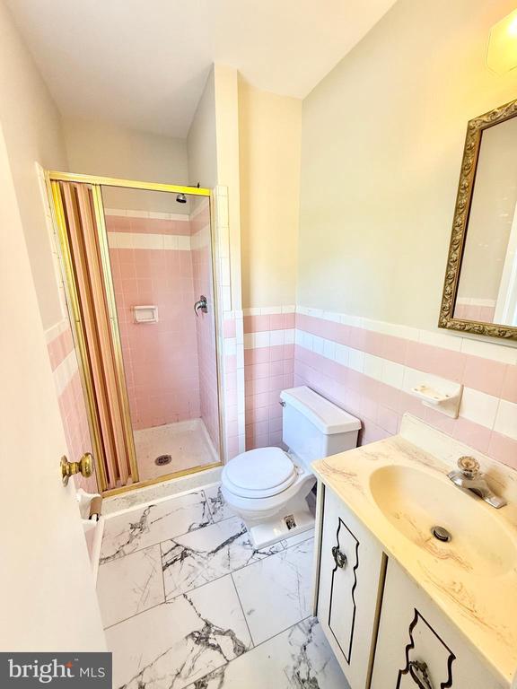 bathroom featuring a stall shower, toilet, vanity, wainscoting, and tile walls