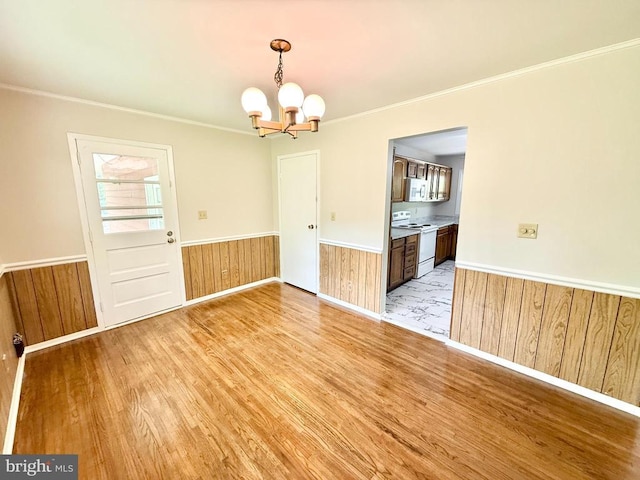 unfurnished dining area with a chandelier, light wood finished floors, a wainscoted wall, ornamental molding, and wooden walls