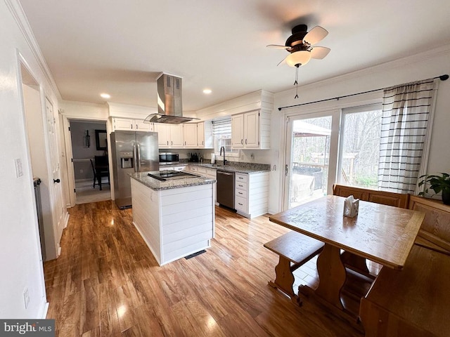 kitchen featuring island range hood, appliances with stainless steel finishes, a sink, ornamental molding, and a center island