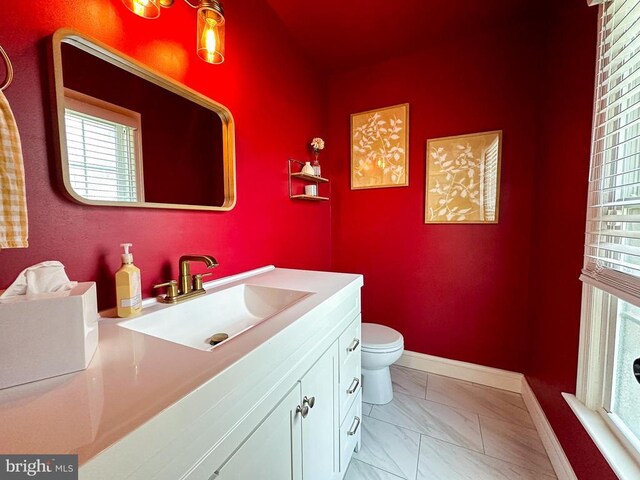 half bath with marble look tile flooring, toilet, vanity, and baseboards