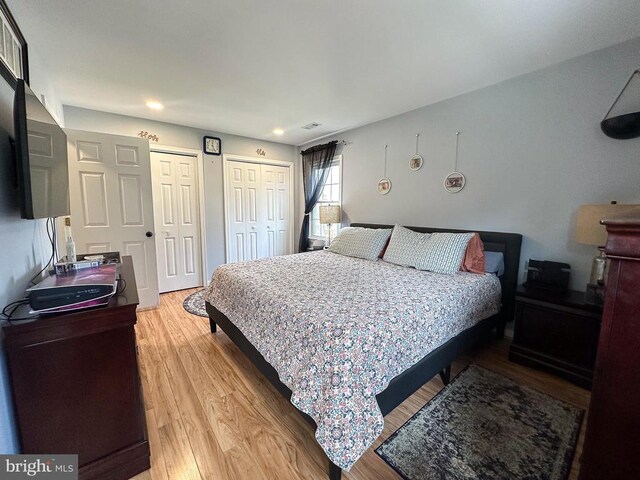 bedroom with two closets, wood finished floors, and recessed lighting