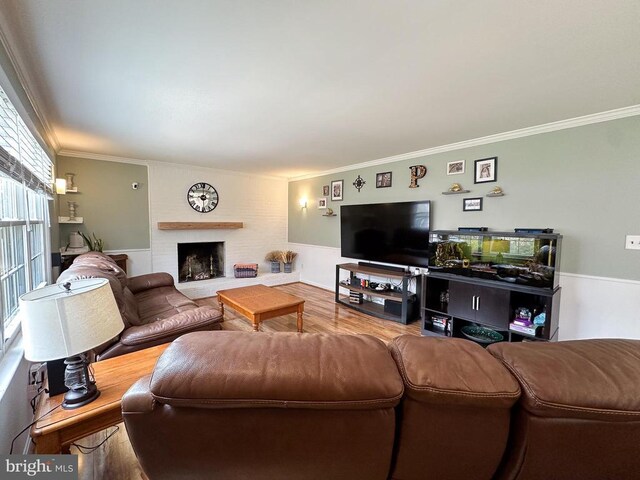 living area with ornamental molding, wood finished floors, and a brick fireplace