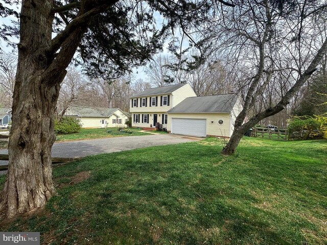 colonial-style house with asphalt driveway, an attached garage, and a front yard