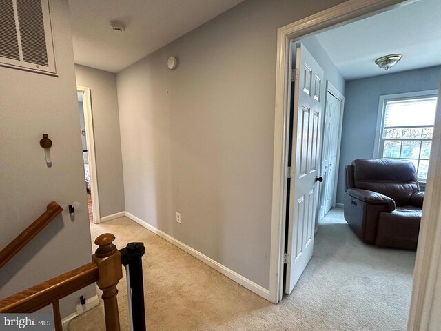hallway featuring light colored carpet, baseboards, and an upstairs landing