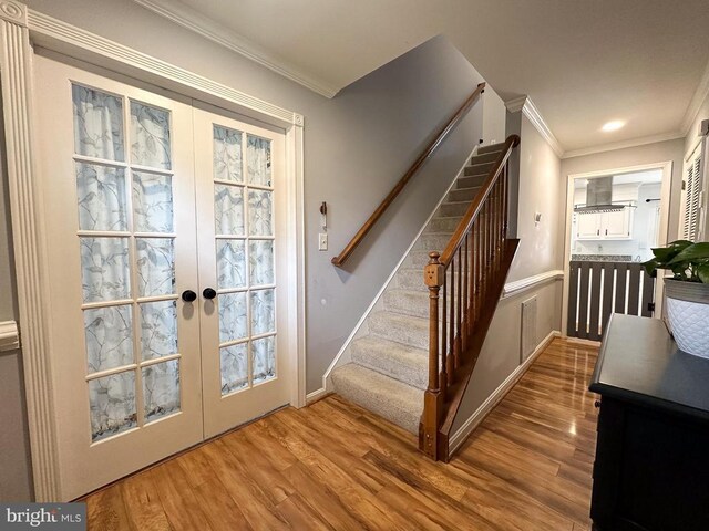 stairway featuring french doors, crown molding, wood finished floors, and baseboards