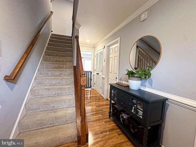 staircase featuring crown molding, wood finished floors, and baseboards
