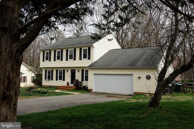 colonial-style house with asphalt driveway, an attached garage, a front yard, and a shingled roof