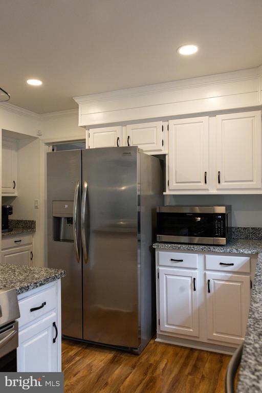 kitchen featuring stainless steel appliances, ornamental molding, white cabinets, dark wood-type flooring, and dark stone countertops