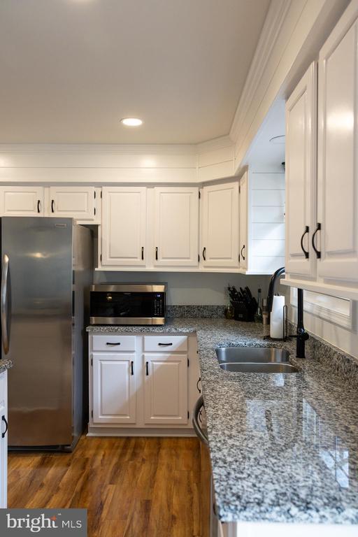 kitchen with appliances with stainless steel finishes, a sink, white cabinetry, stone counters, and wood finished floors