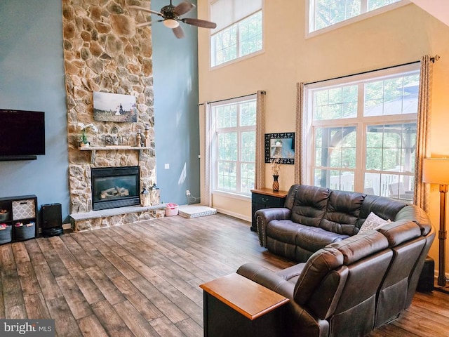  - living room with wood finished floors, ceiling fan, a fireplace, and a high ceiling
