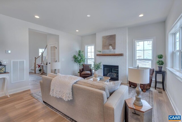 living room with light wood-type flooring, visible vents, a healthy amount of sunlight, and a brick fireplace