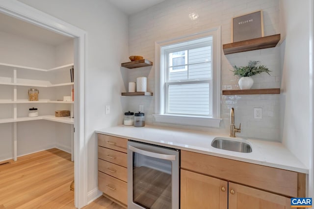 bar with a sink, decorative backsplash, light wood-style floors, and beverage cooler