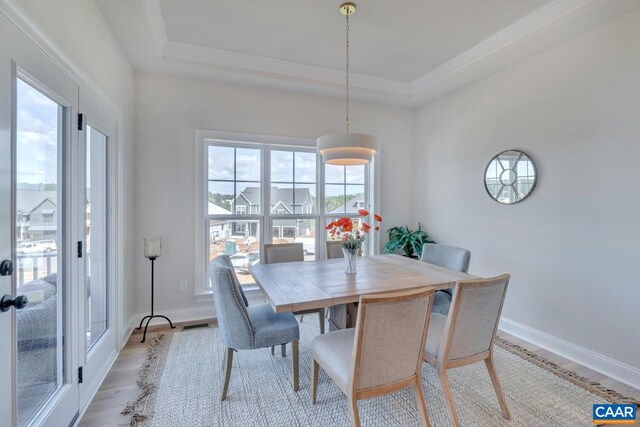 dining area with a tray ceiling, crown molding, light wood-style floors, and baseboards