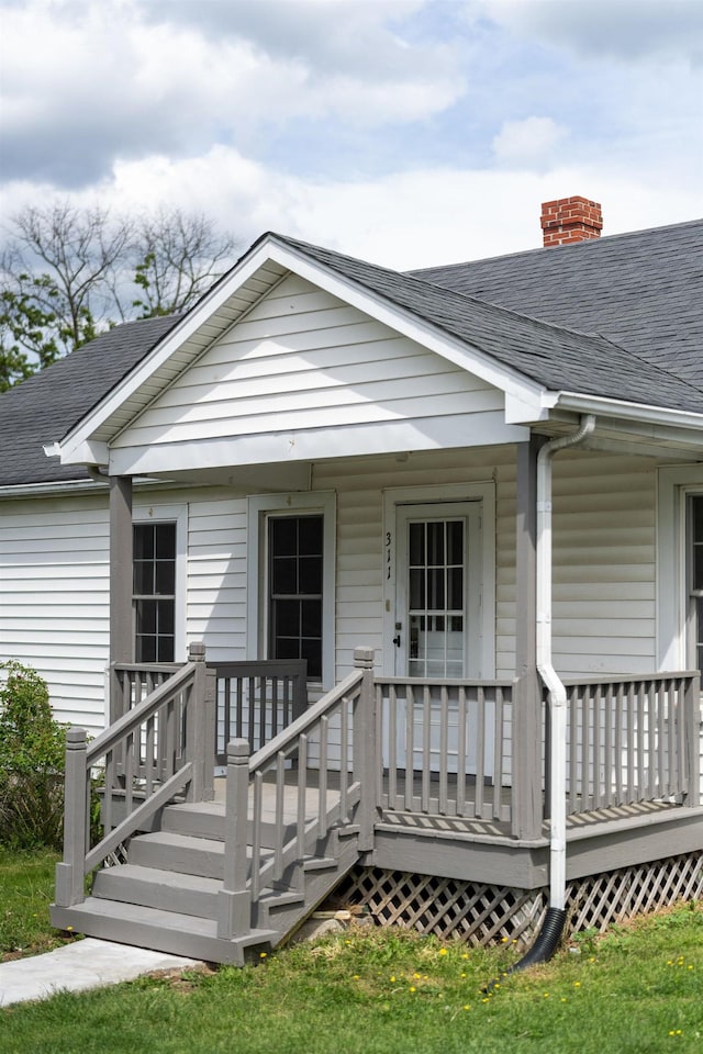 view of front facade with roof with shingles, a chimney, and covered porch