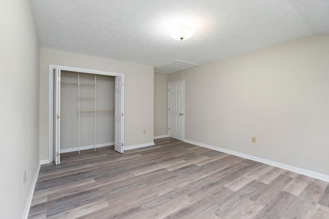 unfurnished bedroom featuring attic access, wood finished floors, a closet, baseboards, and a textured ceiling