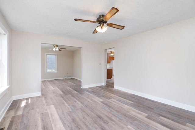 empty room with ceiling fan, light wood finished floors, and baseboards