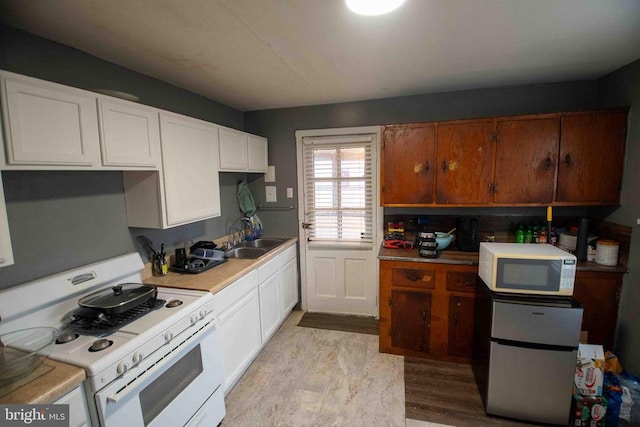 kitchen with white cabinets, light countertops, a sink, and white appliances
