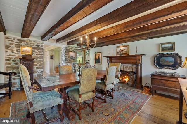  - dining space featuring beamed ceiling, a chandelier, a warm lit fireplace, and hardwood / wood-style floors