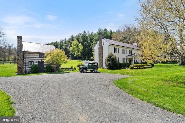  - view of property exterior featuring a chimney, a yard, a standing seam roof, metal roof, and gravel driveway