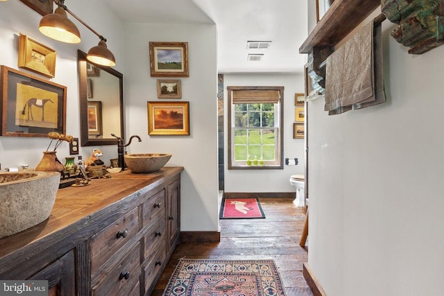  - bathroom featuring a sink, hardwood / wood-style flooring, toilet, visible vents, and baseboards