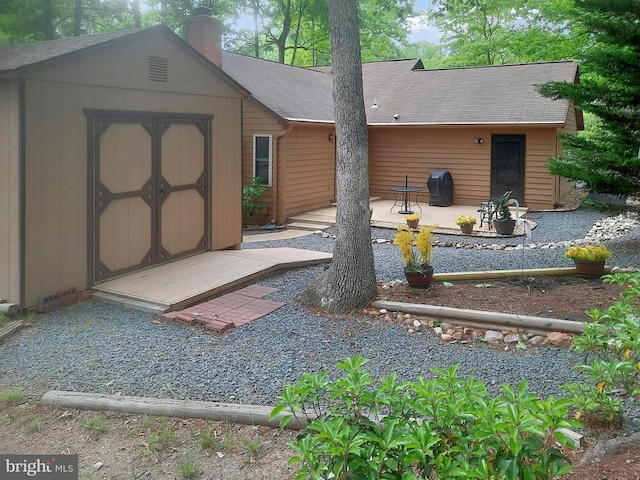 back of property with a shed, a patio, an outdoor structure, a chimney, and roof with shingles
