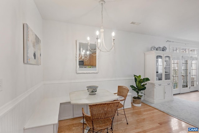 dining space with a chandelier, a wainscoted wall, visible vents, and wood finished floors