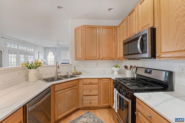 kitchen featuring light stone counters, stainless steel appliances, light wood-type flooring, and a sink