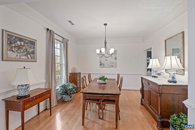 dining room featuring an inviting chandelier, light wood-style flooring, visible vents, and ornamental molding