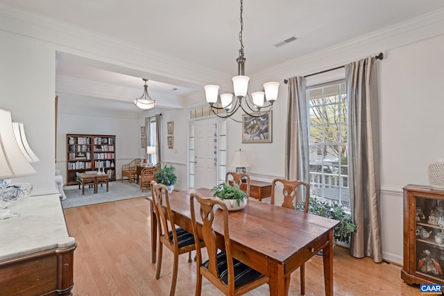 dining area with light wood-type flooring, crown molding, a chandelier, and visible vents