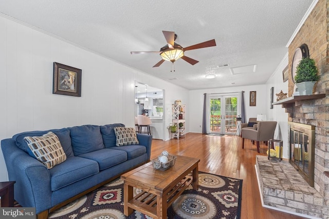  - living area with ceiling fan, a textured ceiling, wood-type flooring, a fireplace, and ornamental molding