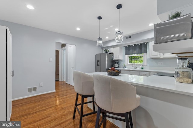 - kitchen featuring stainless steel fridge, white cabinets, light countertops, light wood finished floors, and a breakfast bar area