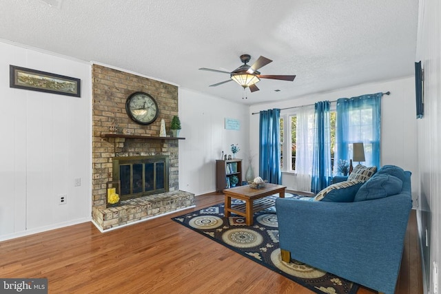  - living room with a textured ceiling, wood finished floors, a ceiling fan, a fireplace, and baseboards