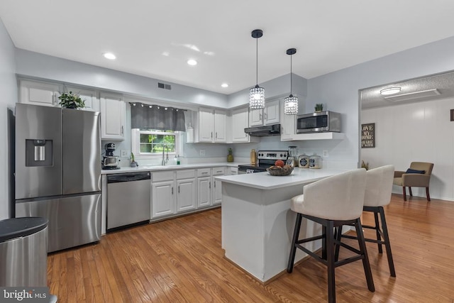  - kitchen with appliances with stainless steel finishes, light countertops, light wood-type flooring, under cabinet range hood, and recessed lighting