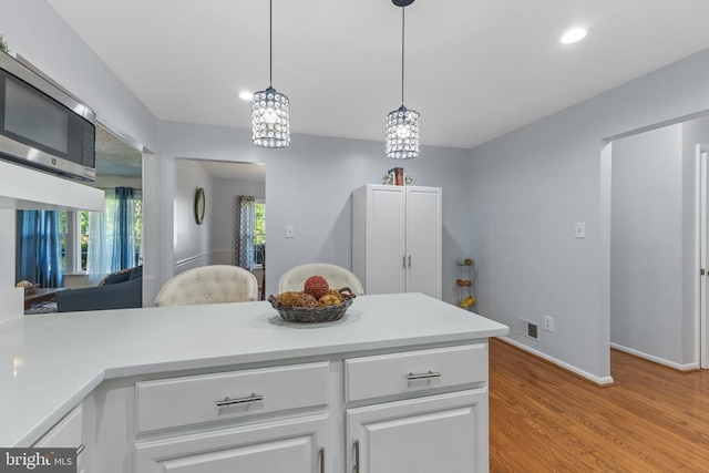  - kitchen featuring stainless steel microwave, light countertops, recessed lighting, white cabinets, and light wood-style flooring
