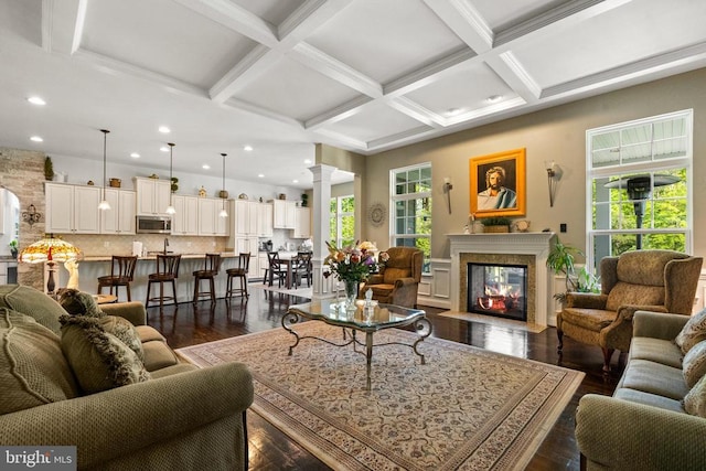  - living area with coffered ceiling, ornate columns, beam ceiling, a multi sided fireplace, and dark wood-style flooring