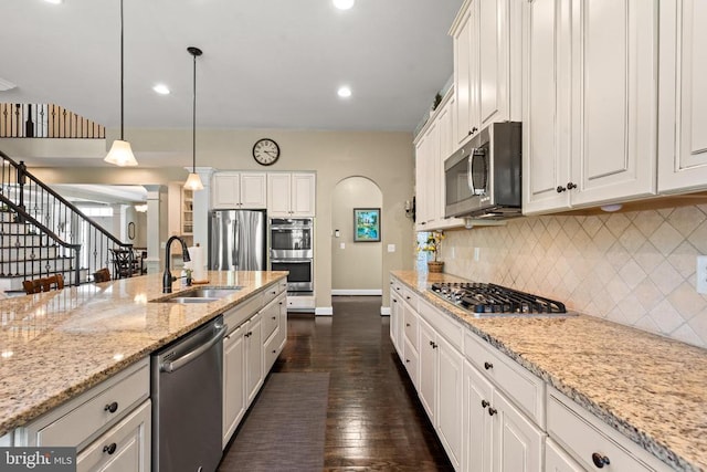 - kitchen featuring stainless steel appliances, arched walkways, dark wood-style flooring, tasteful backsplash, and white cabinets