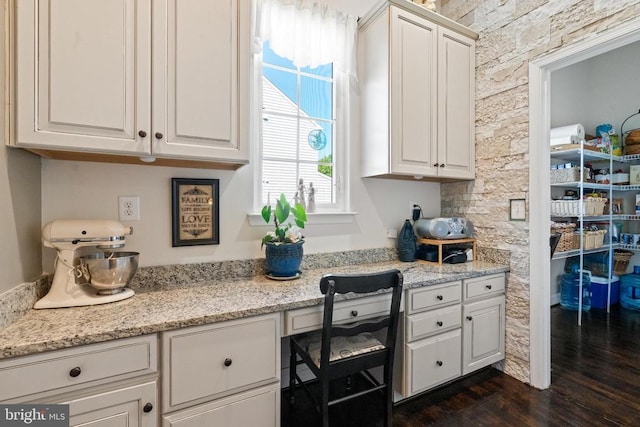 - kitchen with dark wood-style flooring, white cabinetry, built in desk, and light stone countertops