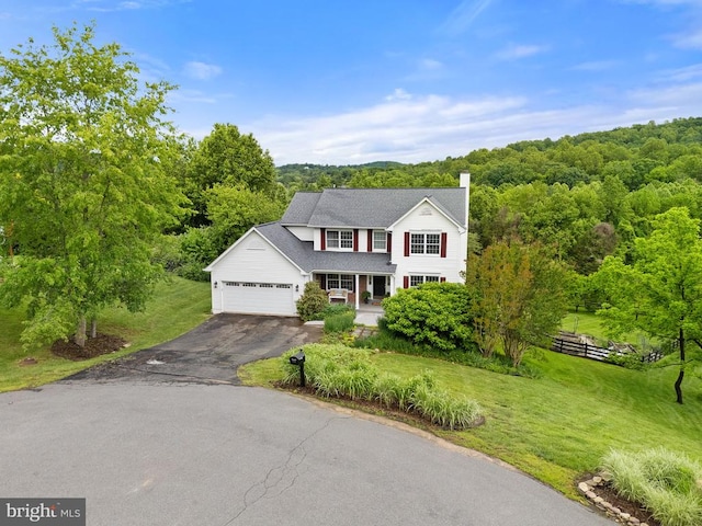  - traditional-style home featuring driveway, a garage, a view of trees, a chimney, and covered porch