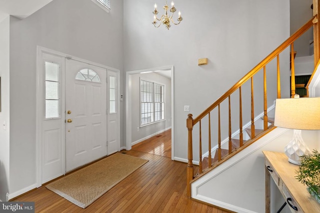  - entryway featuring hardwood / wood-style flooring, stairway, a towering ceiling, a chandelier, and baseboards
