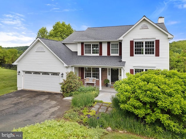  - traditional-style house featuring covered porch, asphalt driveway, roof with shingles, a chimney, and an attached garage