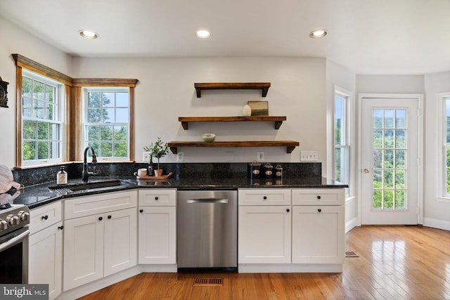  - kitchen featuring appliances with stainless steel finishes, a sink, white cabinets, dark stone counters, and light wood-type flooring