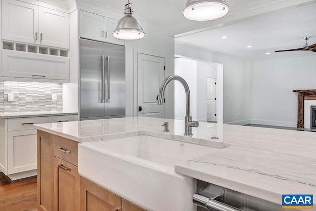 kitchen with hanging light fixtures, stainless steel built in fridge, a sink, light stone countertops, and ornamental molding