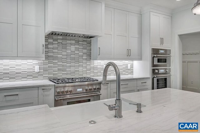 kitchen featuring appliances with stainless steel finishes, tasteful backsplash, light stone countertops, and white cabinetry