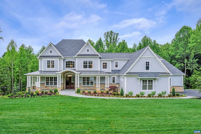 craftsman-style house with a standing seam roof, a front yard, covered porch, stone siding, and roof with shingles